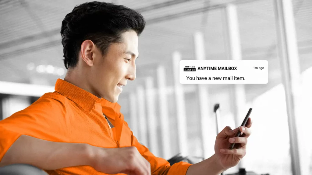 Man holding a mobile phone. The phone has a flowing pop-up showing a “new mail item” Anytime Mailbox notification.