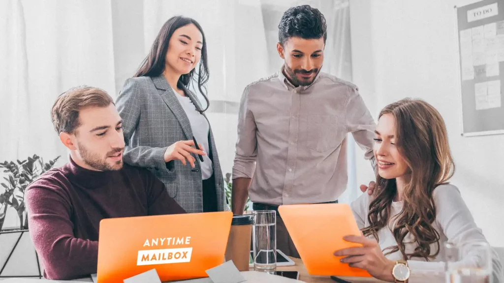 Two men and two women gathered around a table. One man sits in front of a laptop with an Anytime Mailbox label.