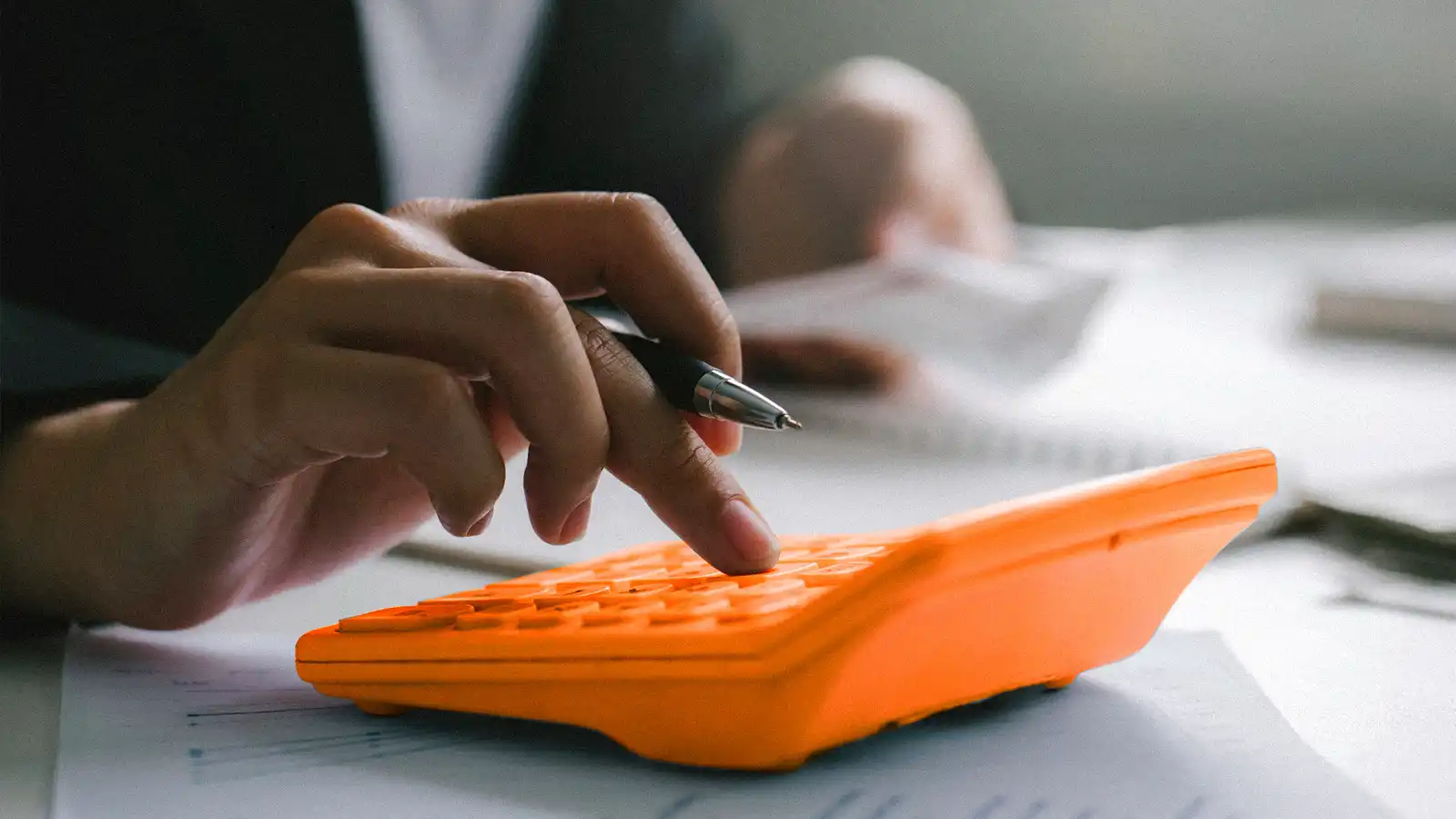 A hand using a calculator. The calculator is placed on top of piles of paper.