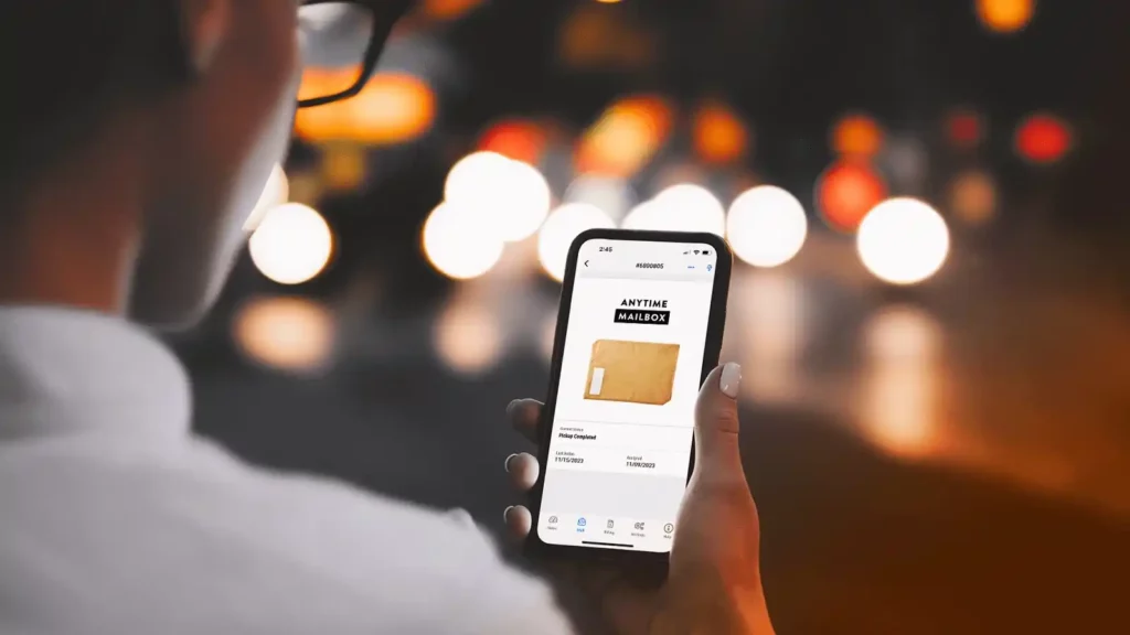 A woman holding a phone showing the Anytime Mailbox app.