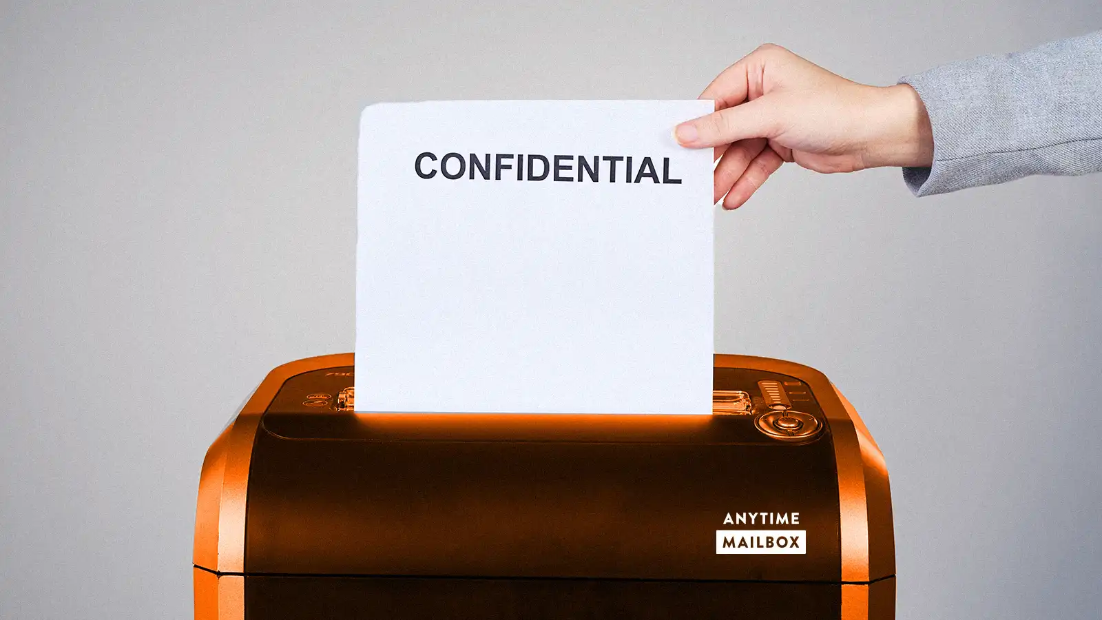 A hand holding a document that says “Confidential” into a shredder. The shredder is labeled Anytime Mailbox.