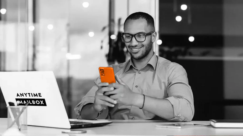 Man sitting in front of laptop, smiling to the phone he’s holding.