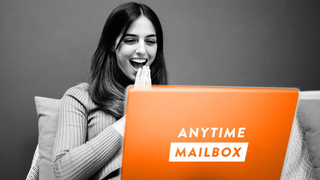 Woman with smiling, with a laptop in front of her. The laptop has an Anytime Mailbox label.