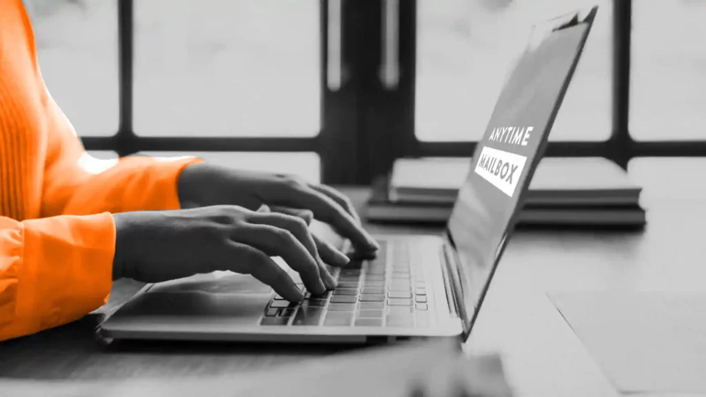 Hands typing on a laptop keyboard. The laptop screen shows the Anytime Mailbox logo.